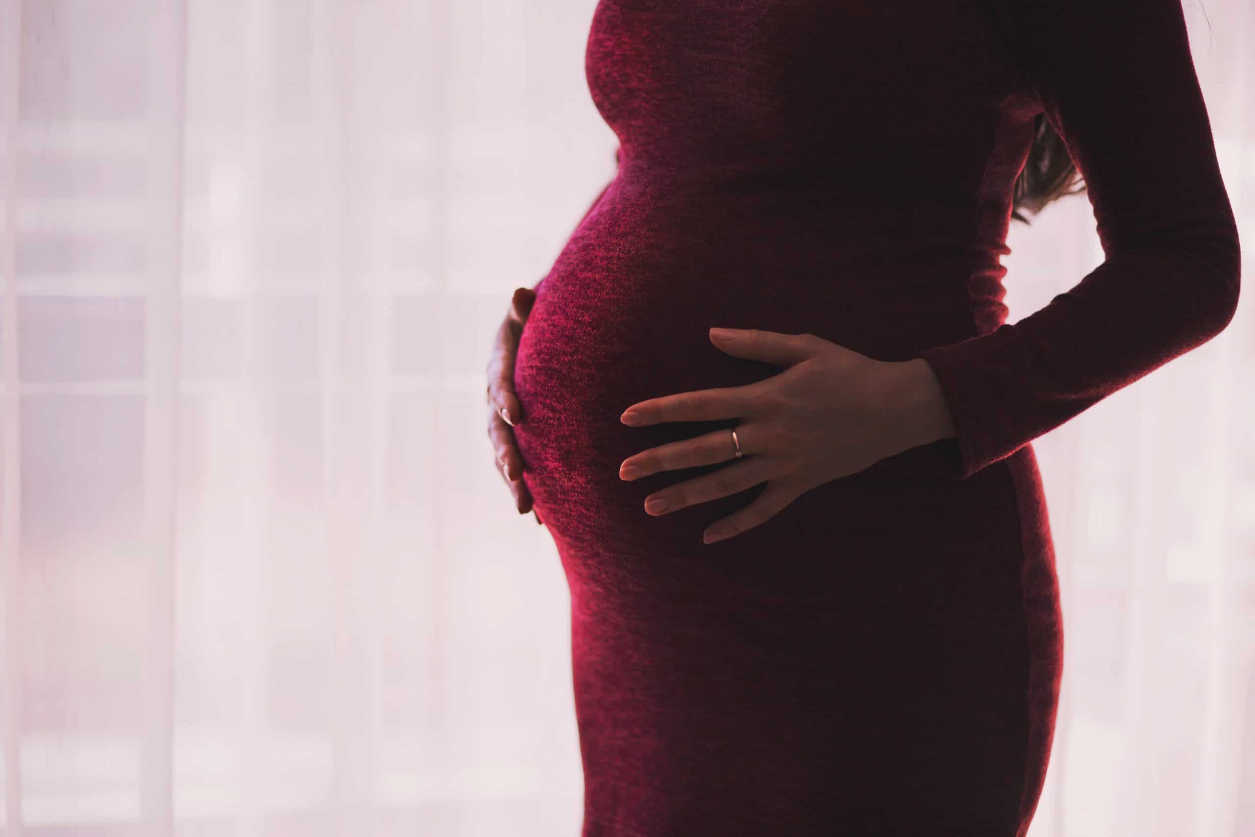 a pregnant woman in a red dress holds her stomach